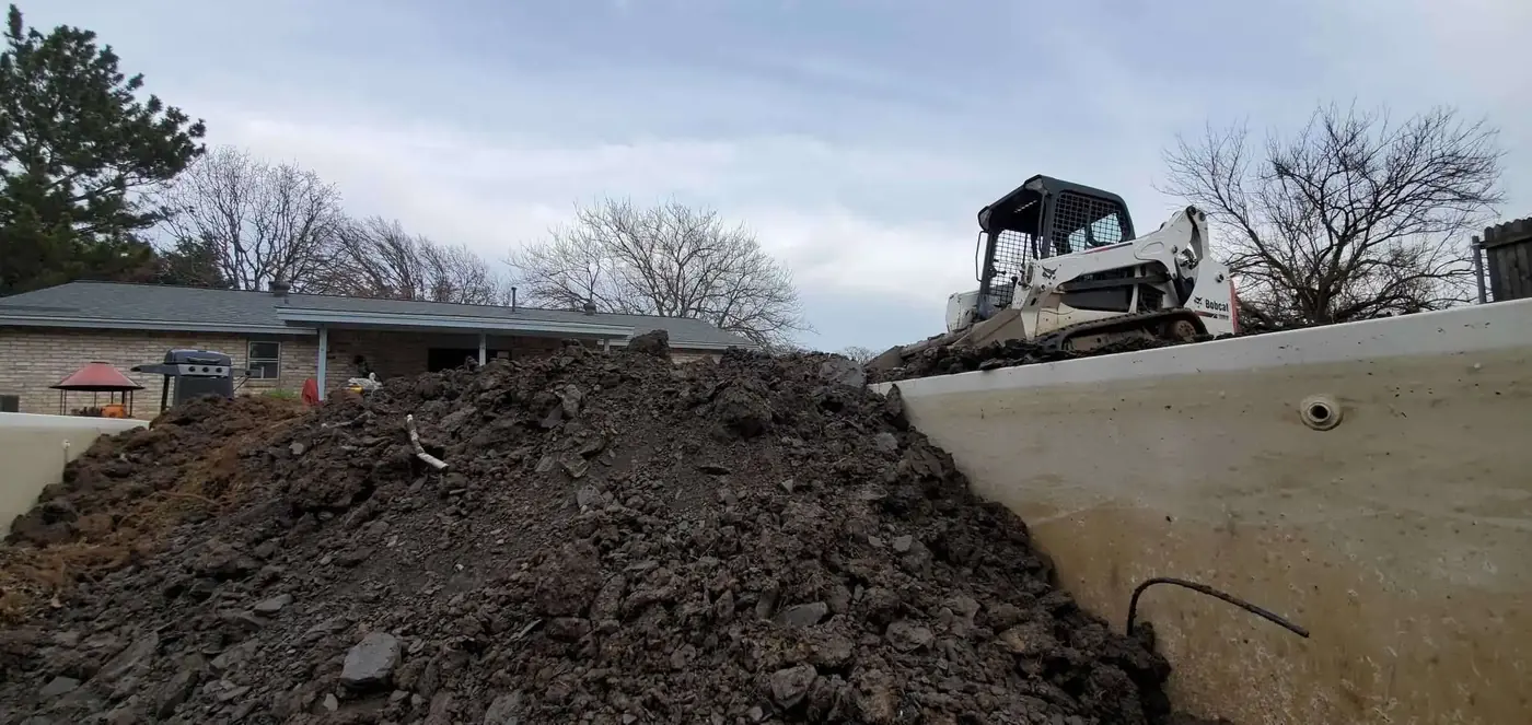 A skid steer moving a delivered pile on a residential lot